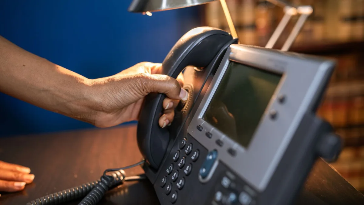 Person lifting the handset of a modern desk phone