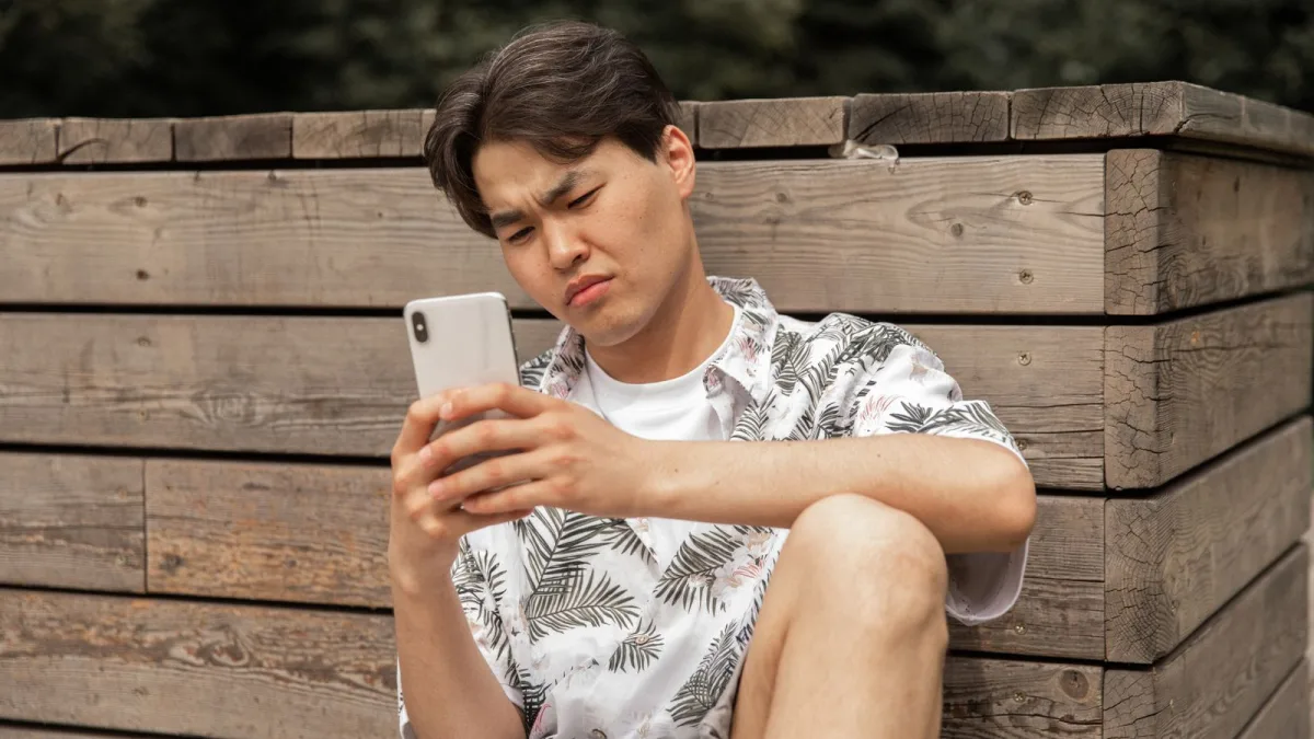Person looking skeptically at a smartphone while seated outdoors