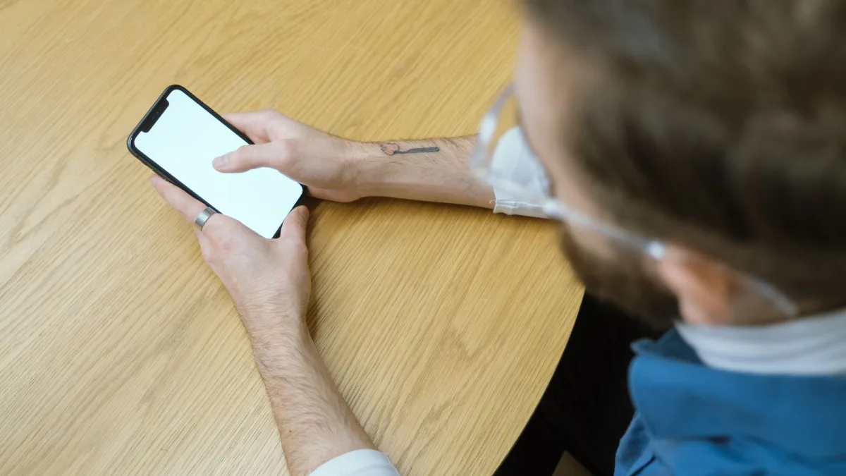 Person seated at a table using a smartphone with a blank screen